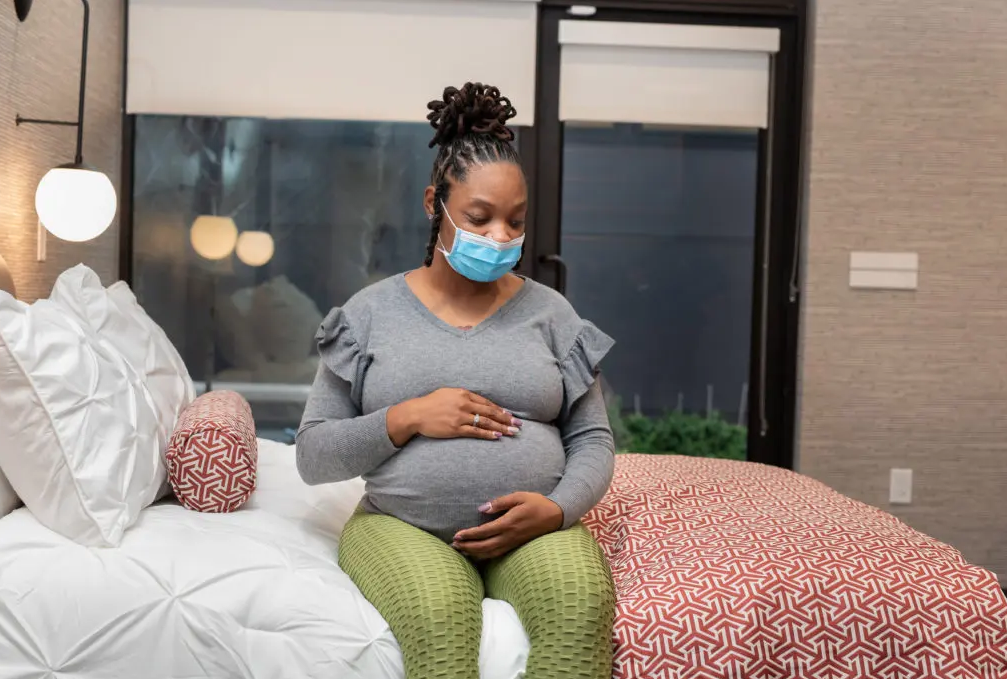 Black pregnant woman sitting on a bed